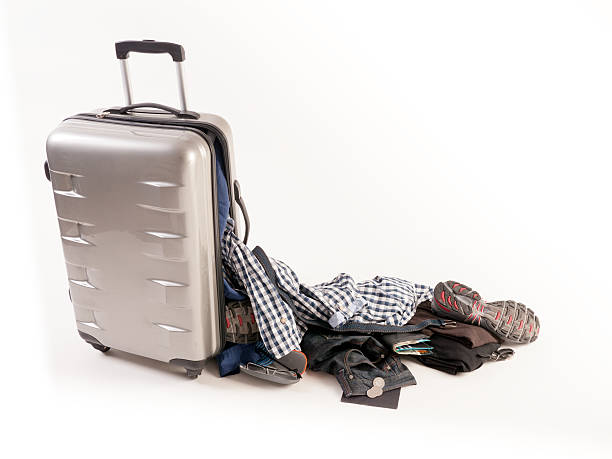 Damaged Suitcase Spinner loses its casual content Damaged silver colored spinner suitcase.The content is casual male clothing dropping on the floor. We see,shirts,coins, shoes and passport broken suitcase stock pictures, royalty-free photos & images