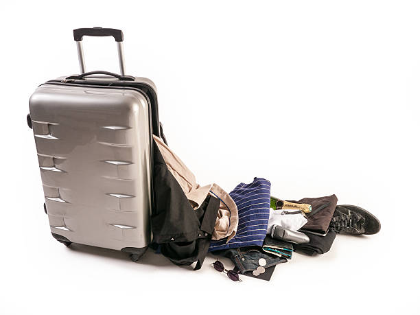 Damaged Suitcase Spinner loses its content Damaged silver colored spinner suitcase. With it's content ,  male clothing dropping on the floor. sun glasses, shaving device kaki pants ,striped shirt and bottle of champagne broken suitcase stock pictures, royalty-free photos & images