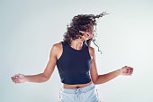 Cropped shot of an attractive young woman flipping her hair and dancing against a gray background in the studio