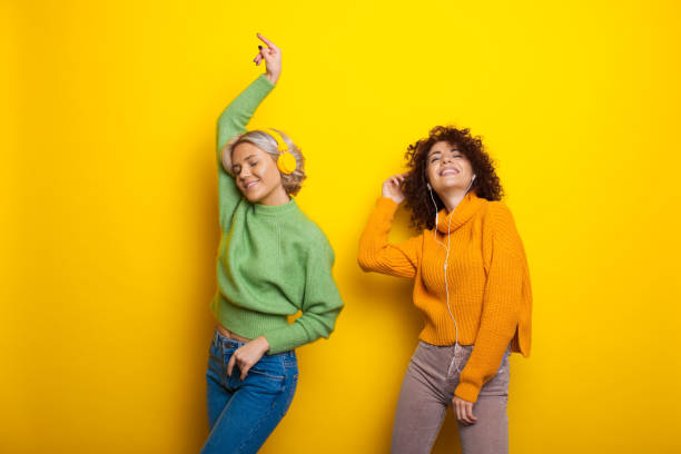 Dancing studio. Beautiful sisters with curly hair listening music. Internet technology. Studio room with yellow color. stock photo