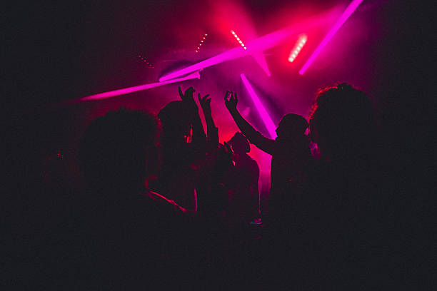 People dancing in a nightclub with smoke machines and strobe lighting around them.