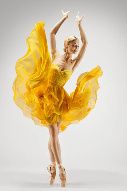 Dancing Woman in Yellow Dress. Ballerina in Shoes Dance Modern Art Ballet over Light Gray Background. Graceful Girl Stretching Hands up stock photo