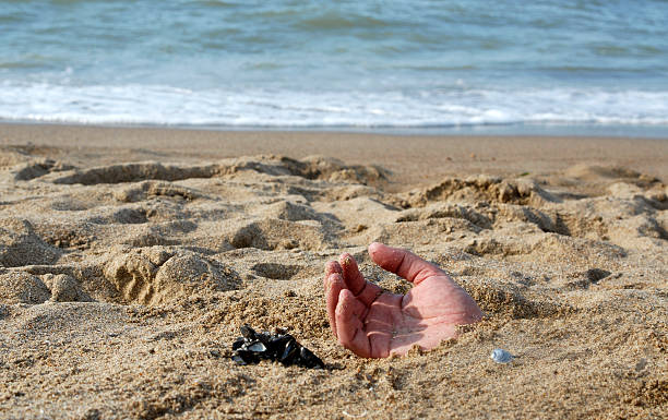 danger of the sea, hand buried in sand stock photo