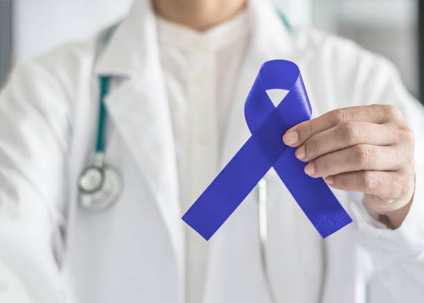 Dark blue ribbon for colon - colorectal cancer awareness on medical doctor's hand support Dark blue ribbon for colon - colorectal cancer awareness on medical doctor's hand support alertness stock pictures, royalty-free photos & images