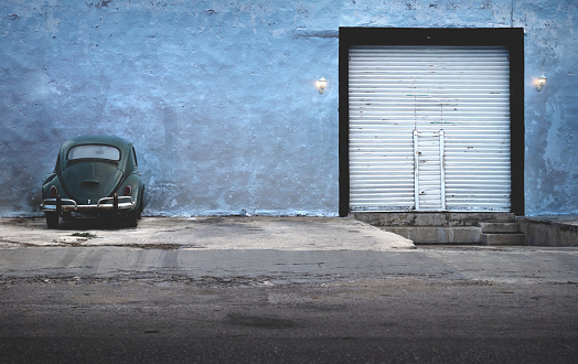 Merida, Yucatan, Mexico - 26 January 2019: Dark green vintage Volkswagen beetle parking at abandoned building with garage gate