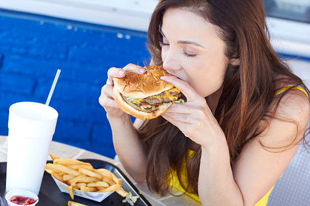 Dark haired woman eating a fast food burger and fries stock photo