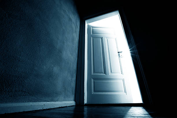Dark hallway with an opened door with bright light coming in stock photo