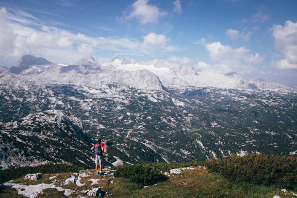 dark-skinned man with a backpack on his back looks at the Dachstein massif in Upper Austria. A purposeful boy in sportswear enjoys nature on the Krippenstein mountain stock photo
