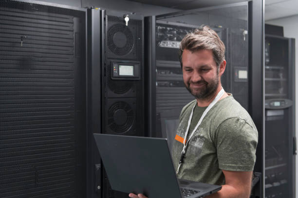 Data Center Engineer Using Laptop Computer Server Room Specialist Facility with Male System Administrator Working with Data Protection Network for Cyber Security or Cryptocurrency Mining Farm. stock photo
