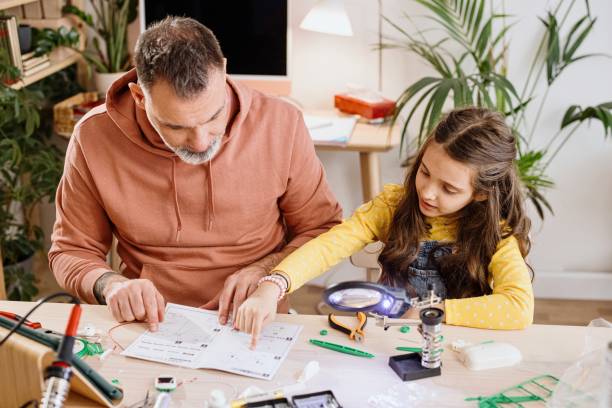Daughter explaining father how to build a robot for a school science project stock photo