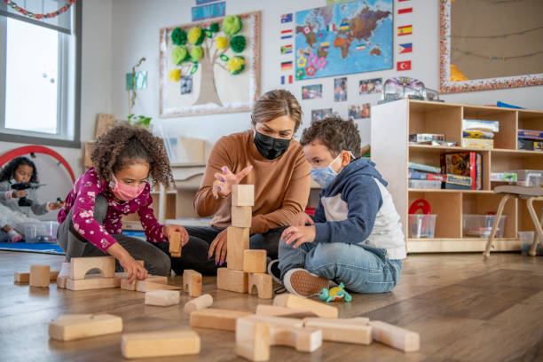 Daycare A teacher helps daycare kids build a structure with wooden blocks on the floor. child care stock pictures, royalty-free photos & images