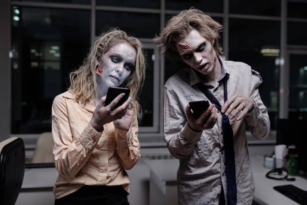 Dead and spooky businesspeople with zombie greasepaint on their faces and hands using smartphones stock photo