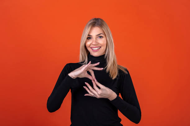 Deaf woman using sign language Portrait Of One Smiling Woman Using Sign Language While Standing Over Red Background. sign language stock pictures, royalty-free photos & images