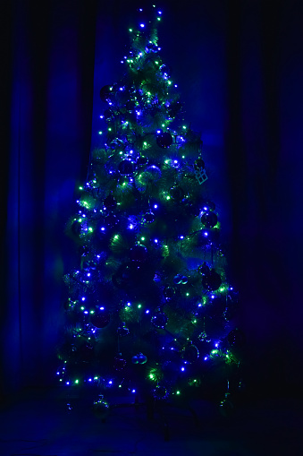 Decorated Christmas tree in the dark, glowing green and blue lights