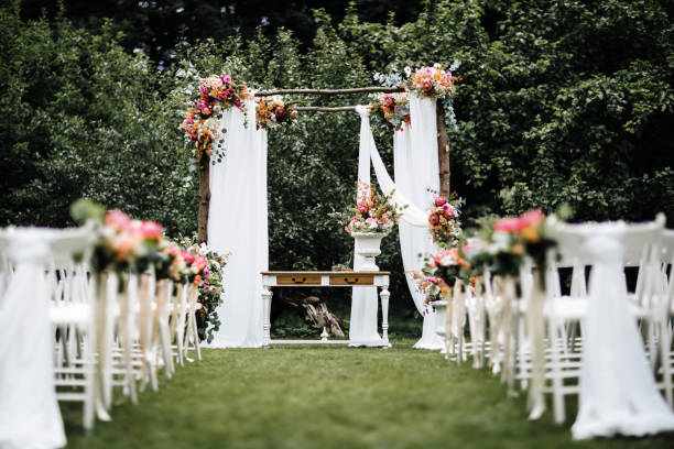 Decorated luxury wedding ceremony place in the garden. White empty chairs and arch decorated with flowers. stock photo