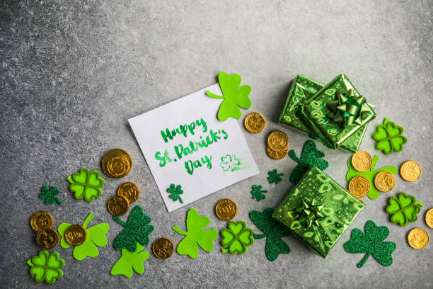 Decorative clover leaves, green gifts box, coins on stone background, flat lay. St. Patrick's Day celebration. Card Happy St. Patrick's Day stock photo