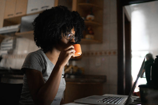 dedykowana młoda kobieta pijąca kawę i czytająca coś na laptopie w domu - curley cup zdjęcia i obrazy z banku zdjęć