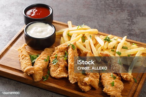 istock Deep-fried chicken strips served with sauces and fries close-up on a wooden tray. horizontal 1360189900