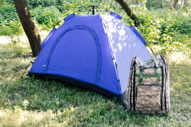 defocus blue open tourist tent standing on green nature background. army backpack. tourism concept. summer vacation in forest, camping. blurred. out of focus - best outdoor tent  個照片及圖片檔