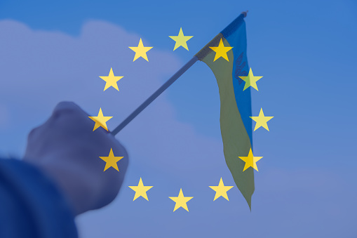 Defocus European union and Ukraine. Large national symbol fluttering in blue sky. Support and help Ukraine, Independence Constitution Day, National holiday. Hand holding flag. Candidate. Out of focus.