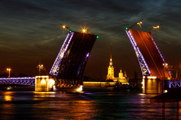 尼瓦河上方凸起的皇宮橋的城市景觀被拆除。  水面上五顏六色的眩光。俄羅斯聖彼德堡的白色夜晚。 - vera pauw 個照片及圖片檔