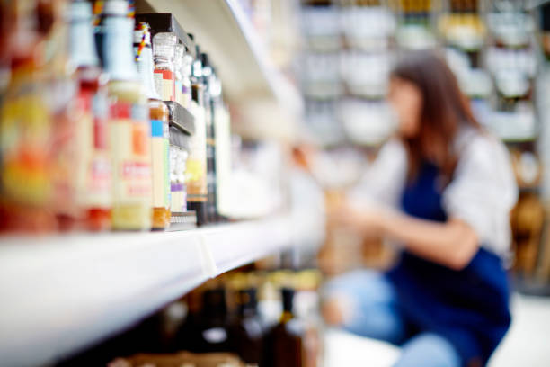 Deli owner kneeling by alcohol bottles on shelves in store stock photo