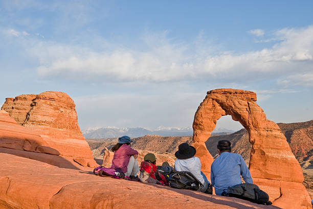 Watching the Sunset on Delicate Arch Arches National Park, Utah, USA - May 16, 2012: Delicate Arch is a 65-foot (20 m) tall Entrada Sandstone arch located in Arches National Park near Moab, Utah, USA. It is the most iconic landmark in the park and is featured on the Utah state license plates and on a postage stamp commemorating Utah's centennial anniversary of statehood in 1996. These people are watching the sunset on the arch. jeff goulden people stock pictures, royalty-free photos & images