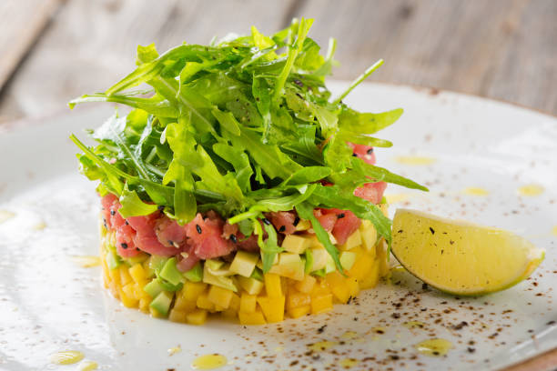 Delicious avocado, mango and raw salmon salad, tartare, served on a white plate with lime Delicious avocado, mango and raw salmon salad, tartare, served on a white plate with lime. Close-up tar stock pictures, royalty-free photos & images