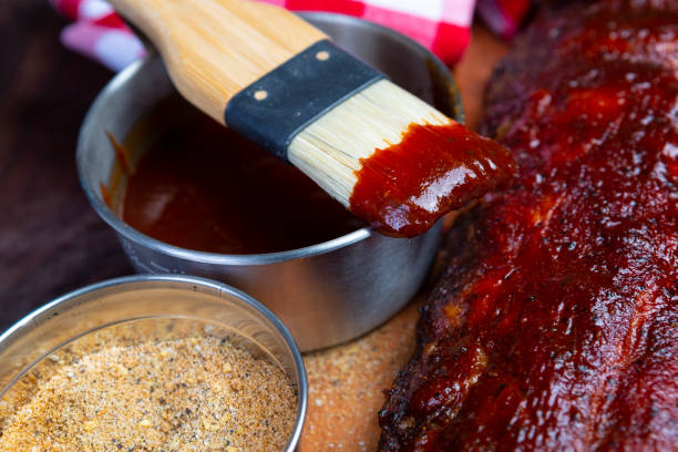 Delicious barbecued ribs seasoned with a spicy basting sauce and spices on an old rustic wooden chopping board in a country kitchen stock photo