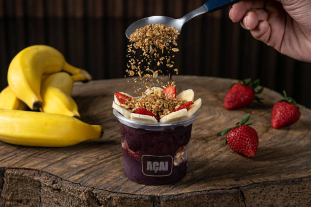 Delicious Brazilian Açaí Cream, in a plastic Cup With Strawberry, banana and granola Topping, in a rustic wooden background. Summer acai smoothie stock photo