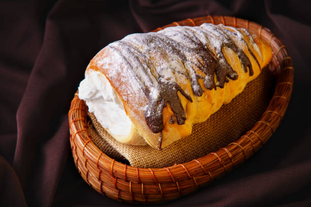 delicious cone-shaped bread rolled up filled with pastry cream covered in homemade chocolate and sugar placed on a rustic container stock photo