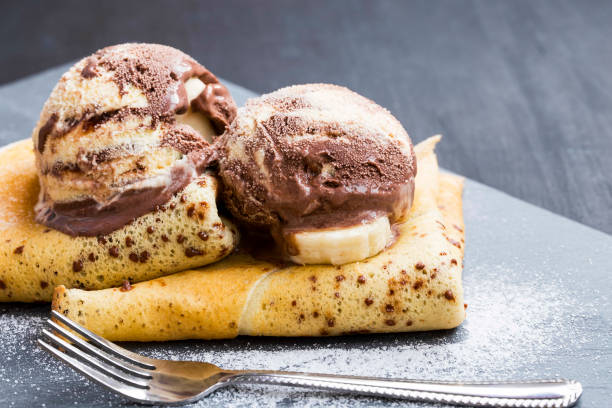 Delicious crepes filled with chocolate sauce, with ice cream scoops on top, elegant tasty dessert dish serving stock photo