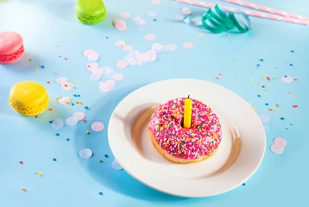 Delicious donut with pink icing and candle confetti macaroons on the background. Birthday concept. stock photo
