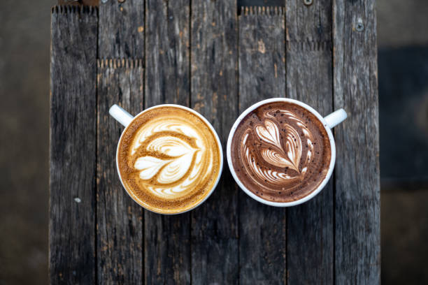heerlijke platte witte koffie en warme chocolademelk met schuim kunst op de top van houten tafel - caffè mocha stockfoto's en -beelden