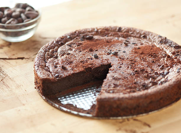 Delicious Flour-less Chocolate Cake A whole chocolate cake dusted with cocoa and cocoa nibs with one slice missing. chocolate cake stock pictures, royalty-free photos & images