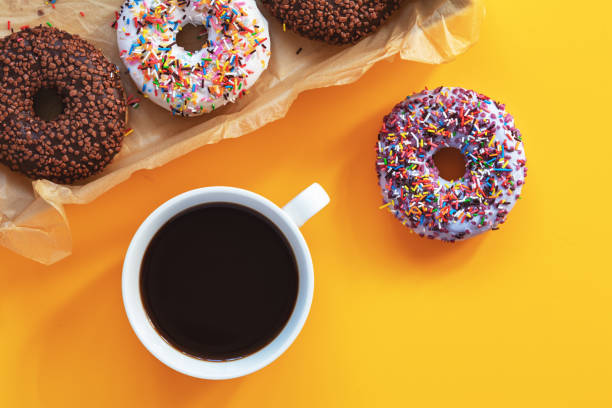 Delicious glazed donuts and cup of coffee on yellow surface stock photo