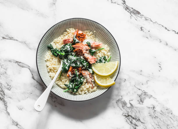 Delicious healthy balanced lunch - grilled salmon, creamy spinach sauce and couscous on a light background, top view stock photo
