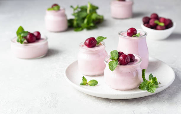 Delicious Italian dessert cherry panna cotta with fresh cherries and mint in jars. Light grey stone background, selective focus. Copy space. stock photo