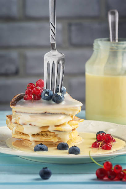 Delicious pancakes with condensed milk and berries. Dessert with blueberries and red currants. A fork is inserted into a stack of freshly fried pancakes. stock photo
