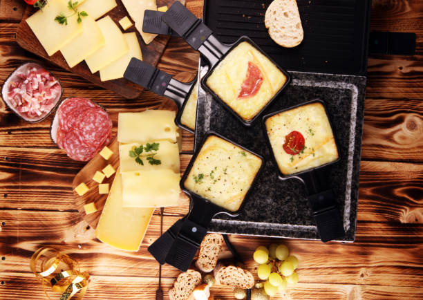 Delicious traditional Swiss melted raclette cheese served in individual skillets with salami. stock photo