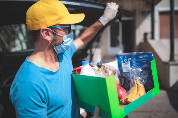 liefermann mit schutzmaske und handschuhen liefern lebensmittel während der sperrung und pandemie. - ehrenamt stock-fotos und bilder