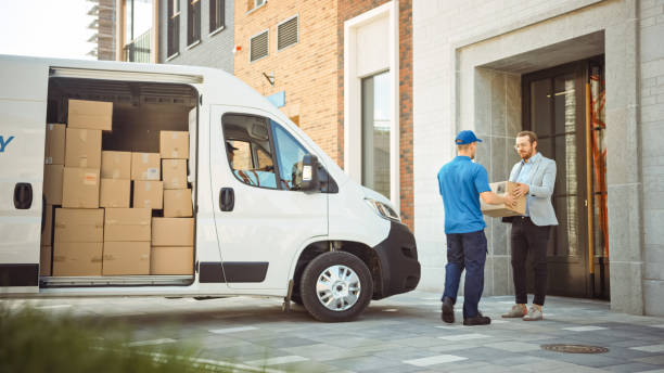 Delivery Man Gives Postal Package to a Business Customer, Who Signs Electronic Signature POD Device. In Stylish Modern Urban Office Area Courier Delivers Cardboard Box Parcel to a Man delivery driver stock pictures, royalty-free photos & images