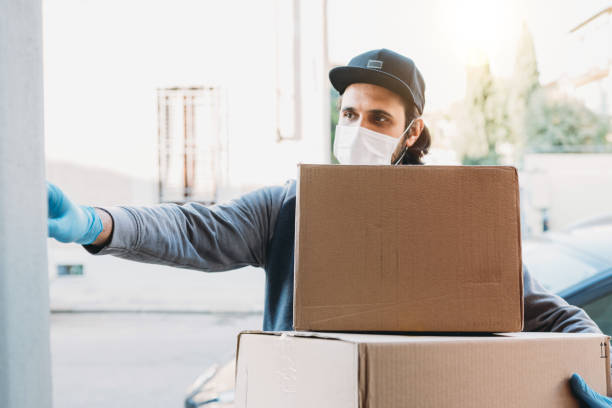 Delivery man is ringing the bell to deliver two cardboard boxes Delivery man is ringing the bell to deliver two cardboard boxes. He's wearing a face mask and protective gloves. home delivery stock pictures, royalty-free photos & images