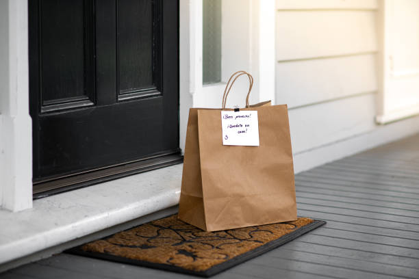 Delivery of food made during quarantine at Covid-19. Food delivered at home with a note written in Spanish "Buen provecho! Quedate en casa!" (translation: Bon Appetite! Stay at home!). Selective focus. home delivery stock pictures, royalty-free photos & images