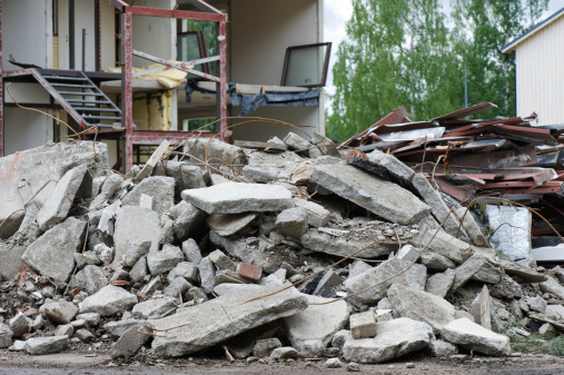 Pile of concrete in front of partially demolished house. Focus on foreground.