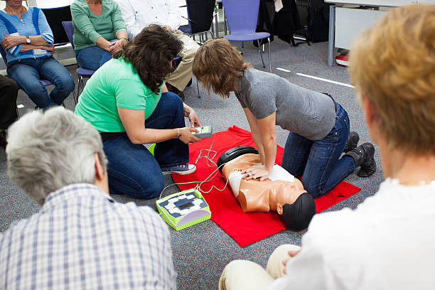 Demonstrating Chest Compressions Female instructors demonstrating chest compressions on a CPR dummy with defibrillator . first aid stock pictures, royalty-free photos & images