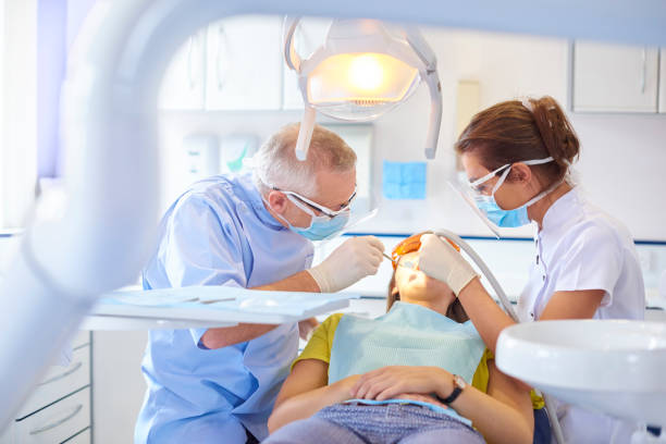 Dental team performing procedure A senior dentist scrapes away some debris from between a patient tooth while the dental nurse applies suction in the mouth to take away any foreign objects. The brightly lit dentist surgery is clean and modern. dental clinic stock pictures, royalty-free photos & images