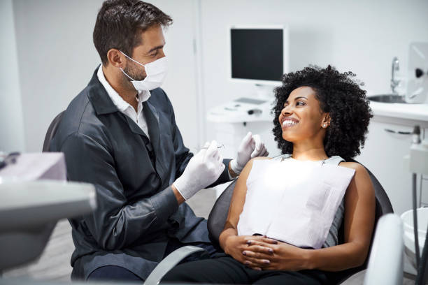 dentist examining smiling female patient in clinic - dental imagens e fotografias de stock