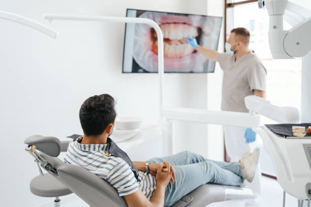 Dentist explaining teeth image on the screen Dentist discussing with laying patient showing the image of his teeth on the screen general view stock pictures, royalty-free photos & images