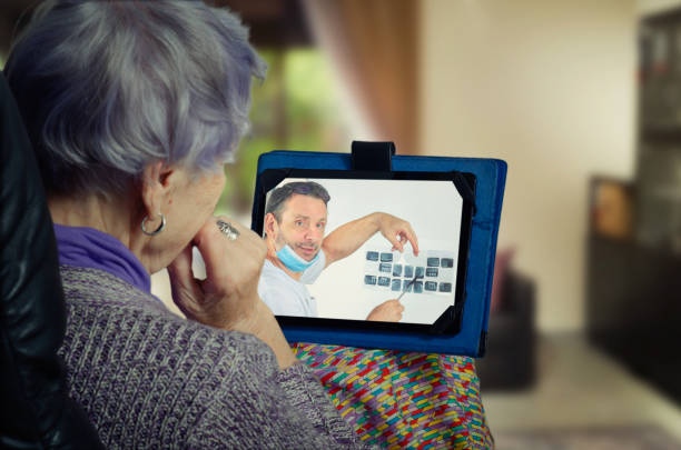 Dentist talks in detail about dental treatment for an elderly patient on a digital tablet screen. stock photo